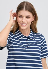 Polo shirt a righe navy e bianche con colletto, quattro bottoni e logo a cuore. Tessuto morbido, maniche corte e vestibilità classica.