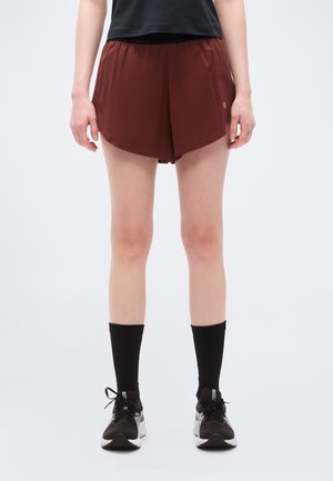 Person iført bordeaux atletikshorts, sorte mellemlange sokker og sorte løbesko, stående mod en ensartet lys baggrund.