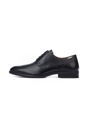 Chaussure habillée pour homme en cuir noir avec fermeture à lacets, talon bas et petite étiquette de marque sur le côté, près du col.