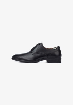 Zapato de vestir para hombre de cuero negro con cierre de cordones, tacón bajo y una pequeña etiqueta de marca en el lateral cerca del cuello.