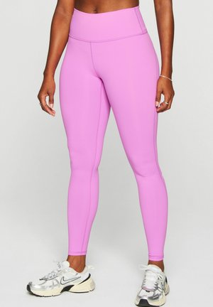 Person wearing high-waisted bright pink leggings with white and silver athletic shoes standing against plain background.