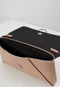 Beige kabelka z umělé kůže s magnetickým uzávěrem, černým textilním interiérem a kapsou na zip, s diagonálním švem.