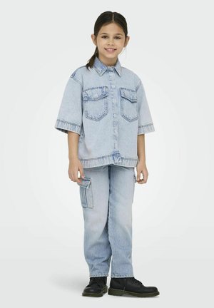 Lichtblauwe denimoutfit met een kortgeplooid overhemd met twee borstzakken en cargobroeken met een ritszak. Zwarte laarzen.
