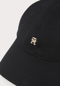 Cappello di lana nera con corona arrotondata e visiera pre-curvata, con un accento del logo in tonalità oro sulla parte frontale e dettagli di cucitura lungo la visiera.