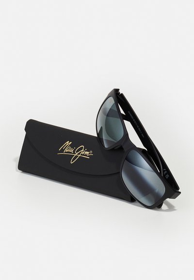 Sorte Maui Jim solbriller med grå linser, der hviler i et sort beskyttelsestilfælde med et gyldent logo. Slank, moderne design og blank overflade.