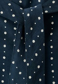 Temno modra tkanina z rebrastim vzorcem, na kateri so majhni beli cvetlični in pikasti vzorci, ter podrobnostjo v obliki spletenga loka.