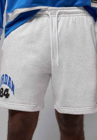 Pantalones cortos de sudadera gris claro con una textura suave, que presentan texto azul "JORDAN" y el número "84" en negro, cintura elástica con cordones blancos.