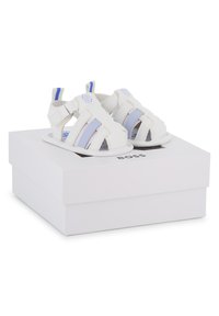 Sandalias de cuero blancas con rayas azules y moradas, diseñadas con dedos abiertos y tiras laterales, exhibidas sobre una caja blanca con logo.