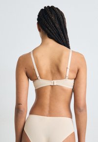 Beige bh met een gladde afwerking, verstelbare banden en een haaksluiting aan de achterkant, gecombineerd met bijpassend naadloos ondergoed.