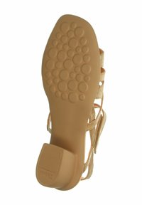 Beżowe sandały z teksturowaną gumową podeszwą o wzorze bąbelków, zapinane w stylu strap, z umiarkowaną piętą. Wykonane z miękkiego materiału w jasnym kolorze.