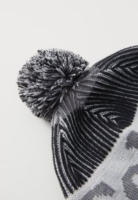 Strikket lue i svart og grått med et teksturert mønster, med en flerfarget pom-pom på toppen. Akenter av vekslende striper.