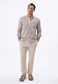Gestreepte blouse met kraag, beige chinos en bruine sandalen. De blouse heeft verticale bruine en witte strepen.