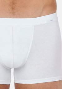 Weiße Baumwoll-Boxershorts mit glatter Textur, passgenauem Design und weichem elastischen Bund. Eine dekorative Naht auf der Vorderseite ist sichtbar.
