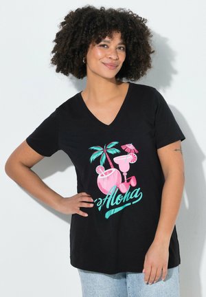 Žena s kudrnatými vlasy, která má na sobě černé tričko s výstřihem do V s růžovými a modrozelenými tropickými nápoji, palmou a nápisem "Aloha", stojící s rukou na bok.