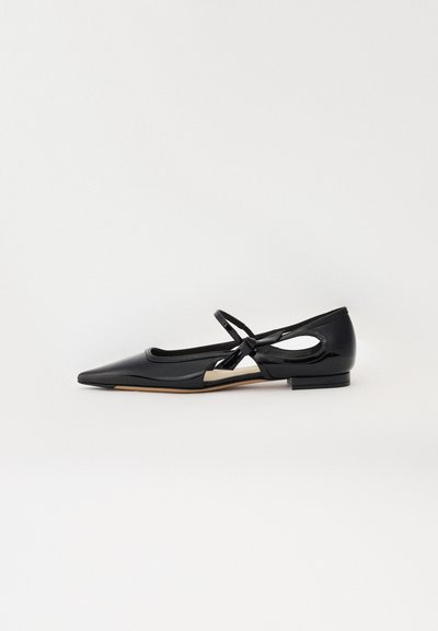Chaussure plate en cuir verni noir avec un bout pointu, des côtés ouverts et un détail en nœud. Elle dispose d'un petit talon et d'une texture lisse.