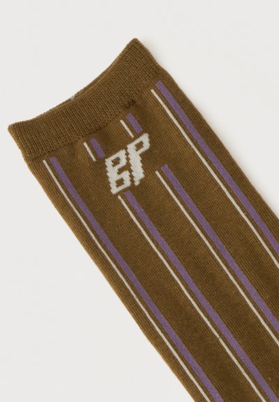 Chaussette marron avec des rayures verticales violettes et blanches et un logo stylisé blanc près du bord-côte sur fond blanc.