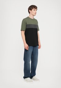 Tricou cu mânecă scurtă în blocuri de culoare verde măsliniu, gri și negru. Material din bumbac, decolteu rotund, cu un detaliu cu logo pe piept.