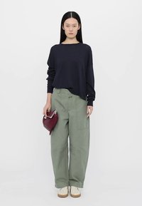 Jūras spēku garām piedurkņu krekls, brīvi pieguļoši olīvu zaļi platšņori, un krējuma krāsas kedas; tur mazu burgundijas krāsas rokassomu.