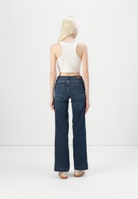 Temno modri denim hlače s razširjenim hlačnicam, dvema zadnjima žepoma, znamčni usnjeni trak na pasu, v kombinaciji z belo brezrokavnik.