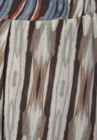 Textiel met een herhaald patroon van verlengde bruine en beige strepen met blauwe en oranje accenten op een lichte achtergrond.