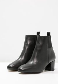 Bottines en cuir noir avec une finition lisse, bout rond, panneaux latéraux élastiques et talon semi-large. Design simple et minimaliste.