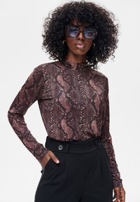 Bluzka z długim rękawem w wężowy wzór, z wysokim dekoltem w odcieniach brązu i czerni, zestawiona z czarnymi, wysokim stanem spodniami.