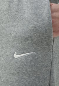 Grå sweatshirt gjord av mjukt tyg, med en broderad vit Nike-logga på vänster sida, med en enkel och ren design.