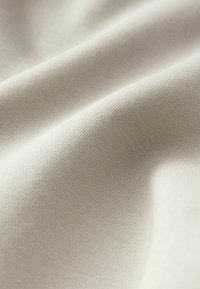 Tela beige clara con una textura suave, que presenta un fino patrón de canales, se pliega suavemente, mostrando su flexibilidad y suavidad.