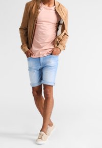 Vaaleanruskea mokkanahkainen pommitustakki vaaleanpunaisen t-paidan päällä, yhdistetty farkkushortseihin. Beigeä tennariparia täydentää rentoa asua.