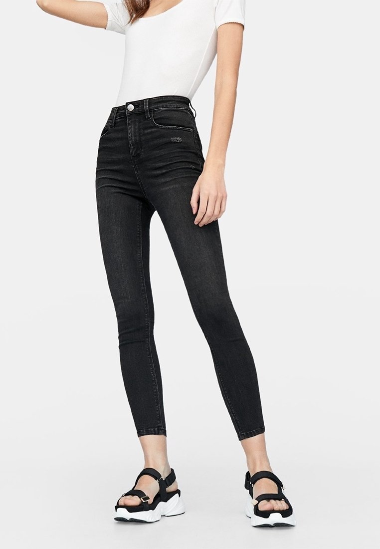 Jeans ajustados de tiro alto en negro, confeccionados en denim, que cuentan con un diseño clásico de cinco bolsillos y líneas limpias. Combinados con sandalias negras.