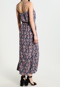 Robe maxi fleurie à fines bretelles, avec un fond bleu marine orné de petites fleurs rouges et blanches ; coupe ample, taille cintrée.