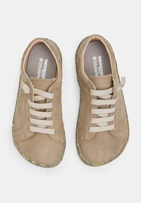 Adidași din piele bej cu suprafață texturată, vârf rotund, șireturi elastice bej și talpă din cauciuc verde subtilă; branț ortopedic vizibil în interior.