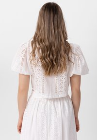 Biała suknia z haftowanymi detalami, krótkimi bufiastymi rękawami i dopasowanym gorsetem, prowadzącym do zwiewnej spódnicy. Gładka tekstura, lekki materiał.