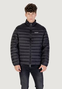 Chaqueta de plumón negra con patrón acolchado horizontal, cuello alto, cremallera frontal y detalle de logo en el pecho. Tejido suave y ligero.