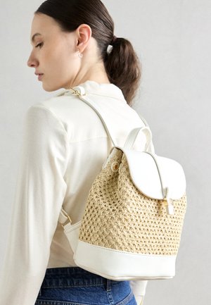 Sac à dos en paille tissée avec une base en simili cuir crème et une fermeture à rabat, doté de quincaillerie dorée et de bretelles réglables.