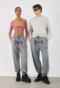 Rød rutete crop top med snøring i halsen, parret med grå joggebukser med rød grafisk tekst. Modellen har på seg svarte chunky sneakers.
