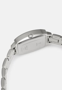 Orologio in acciaio inox argentato con cassa rettangolare, corona testurizzata e cinturino a maglie. Il retro presenta incisioni e una finitura lucida.