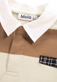 Poloshirt in hellgrünen und braunen Streifen, mit weißem Kragen, einer horizontalen Knopfleiste und einem kleinen schwarzen Aufnäher mit Karomuster.