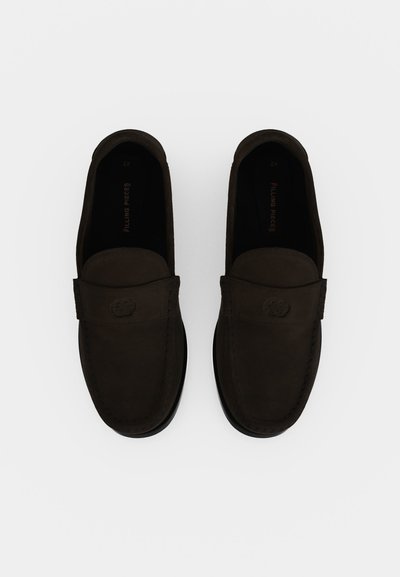 Ζευγάρι σκούρα καφέ παπούτσια τύπου loafers χωρίς κορδόνια με στρογγυλεμένη μύτη και ραμμένη λεπτομέρεια σε λευκό φόντο.