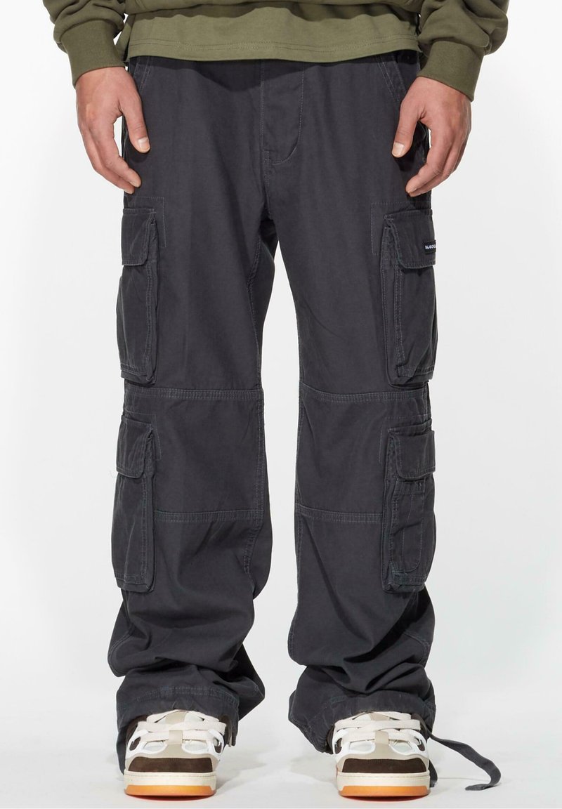 Dark cargo pants featuring multiple side pockets, a loose fit, and durable cotton material. Paired with white and brown sneakers.