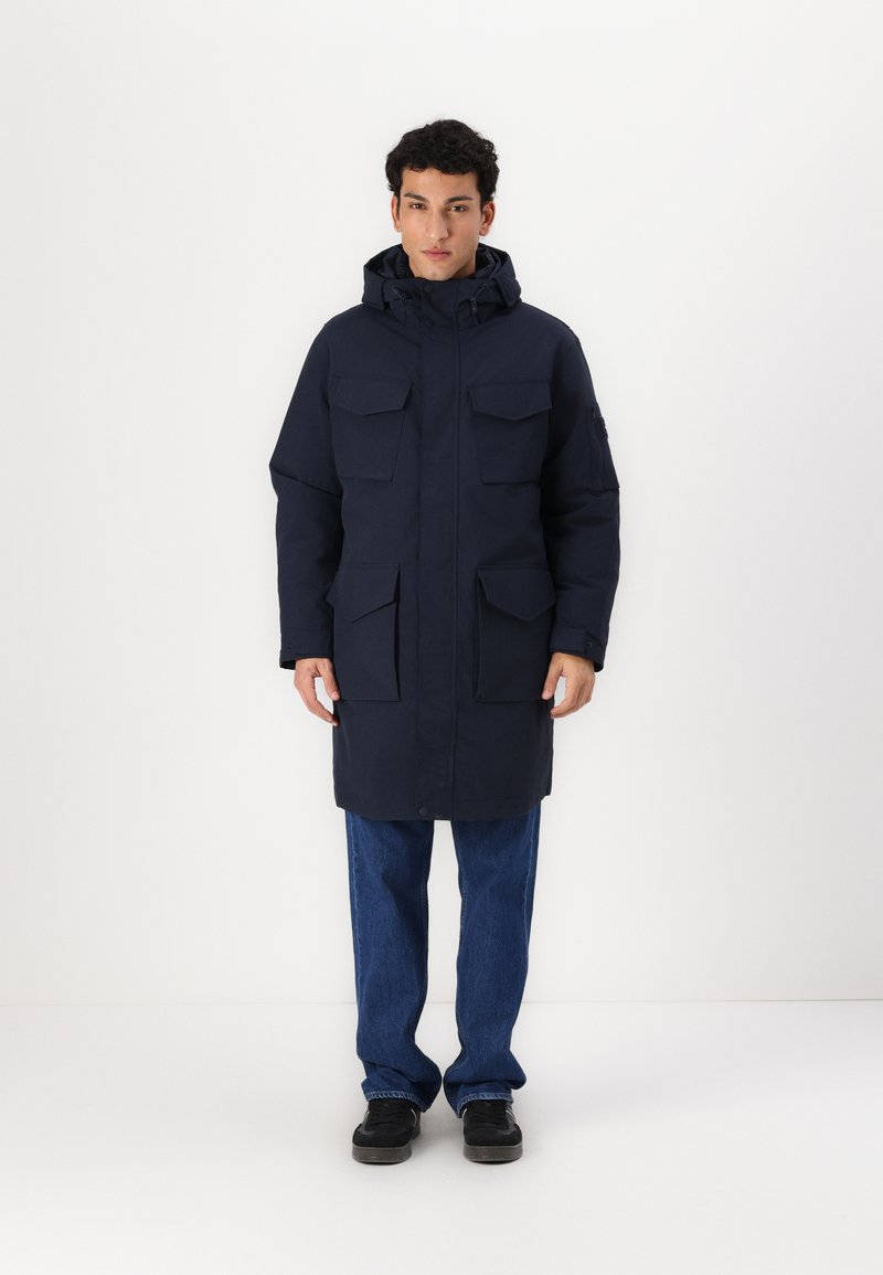Parka marine imperméable avec capuche, dotée de plusieurs poches poitrine et latérales, d'une coupe mi-longue et d'une fermeture à boutons-pression à l'avant.