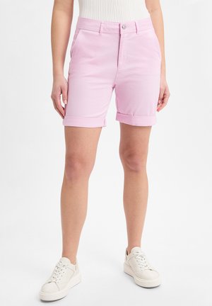 Rosa Baumwollshorts mit aufgeschlagenem Saum, seitlichen Taschen und Knopfverschluss vorne, kombiniert mit weißen Sneakers.