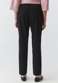 Black, straight-leg trousers with a smooth texture and elastic waistband, featuring two back pockets and paired with black flats.