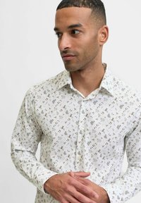 Valkoinen kauluspaita, jossa on pieniä kukkakuosia vihreässä, beigeessä ja sinisessä. Ominaisuuksina säännömmäinen kaulus ja pitkät hihat.