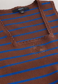 Haut en tissu côtelé marron avec des rayures horizontales bleues, encolure carrée avec bordure en dentelle et une petite broderie de soleil sous le col.