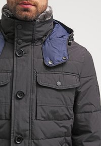 Kurtka pikowana w ciemnoszarym kolorze z kołnierzem wyłożonym futrem i niebieskimi akcentami. Posiada cztery przednie kieszenie oraz czarne zapięcia na guziki.