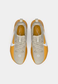 Chaussures de sport beige et orange avec une tige texturée, arborant un logo Nike blanc, un système de laçage et un col rembourré pour le confort.