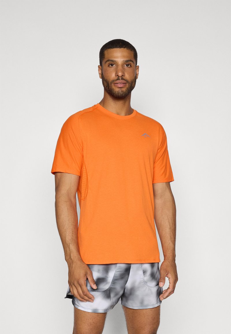 Maglietta sportiva arancione a maniche corte realizzata in tessuto traspirante con un logo discreto; abbinata a pantaloni corti grigi con effetto tie-dye e dotati di tasche.