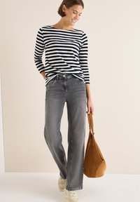 Langærmet navy- og hvidstribet top parret med grå wide-leg jeans og cremede sneakers; holder en brun ruskinds taske. Neutral baggrund.