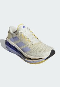 Scarpa sportiva bianca e viola chiaro con tomaia testurizzata, branding a tre strisce e suola spessa con accenti gialli e neri.